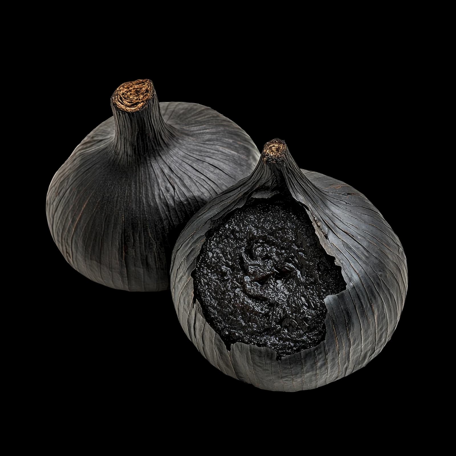Two whole black garlic bulbs, one torn open to show the soft, jammy black cloves inside